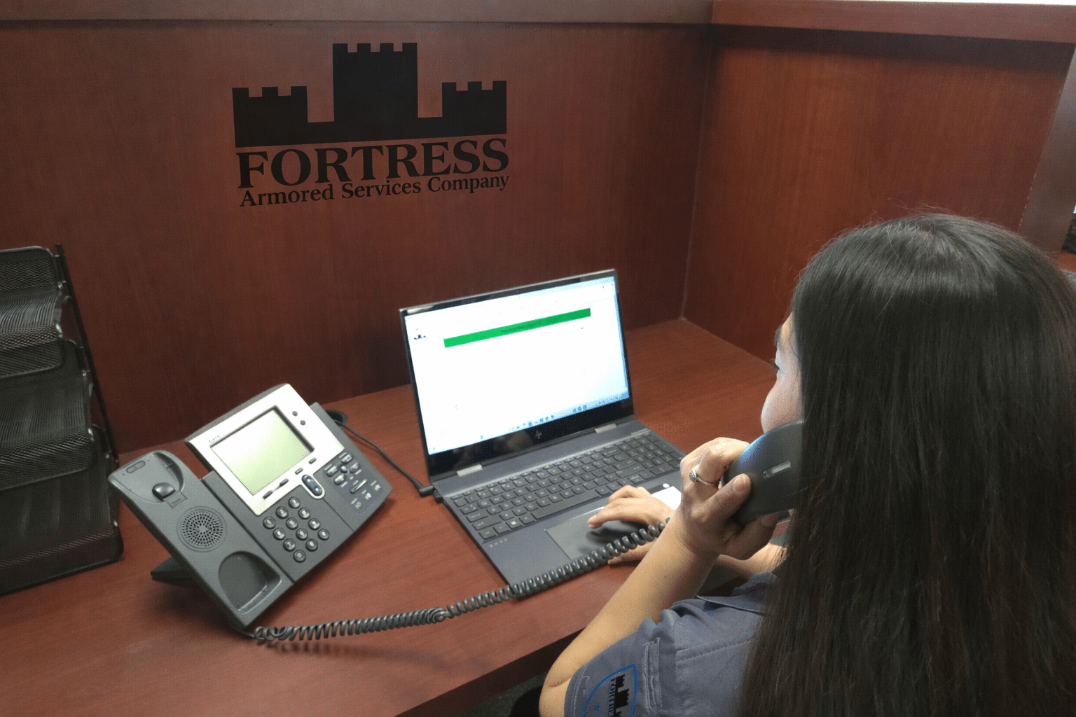 Woman at desk using laptop and phone.